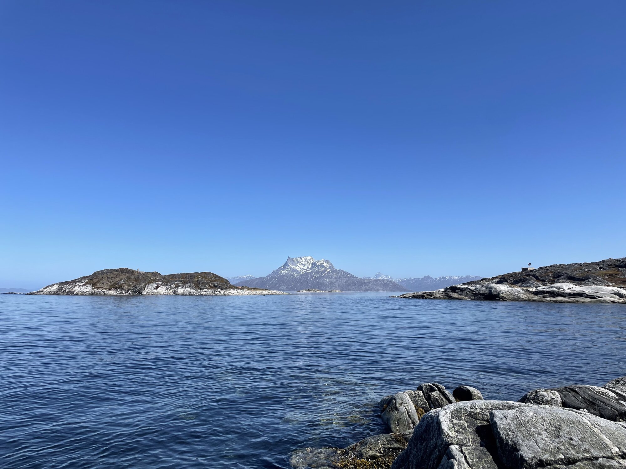 Fjorden set fra Qernertunnguit med roligt vand og et snebelagt bjerg i baggrunden.