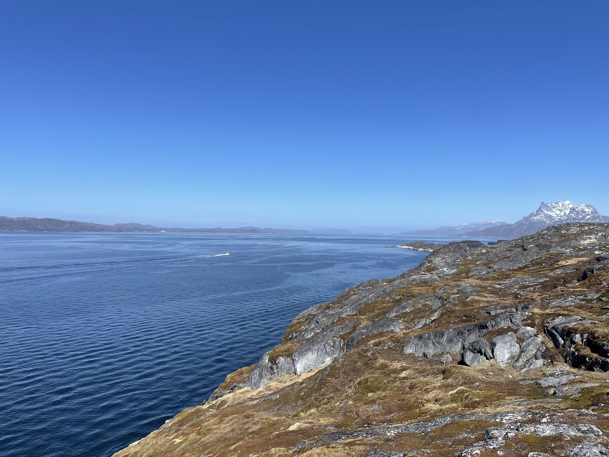 Panoramaudsigt over fjorden fra Qernertunnguit med en lille båd på det spejlblanke vand og fjelde i horisonten.