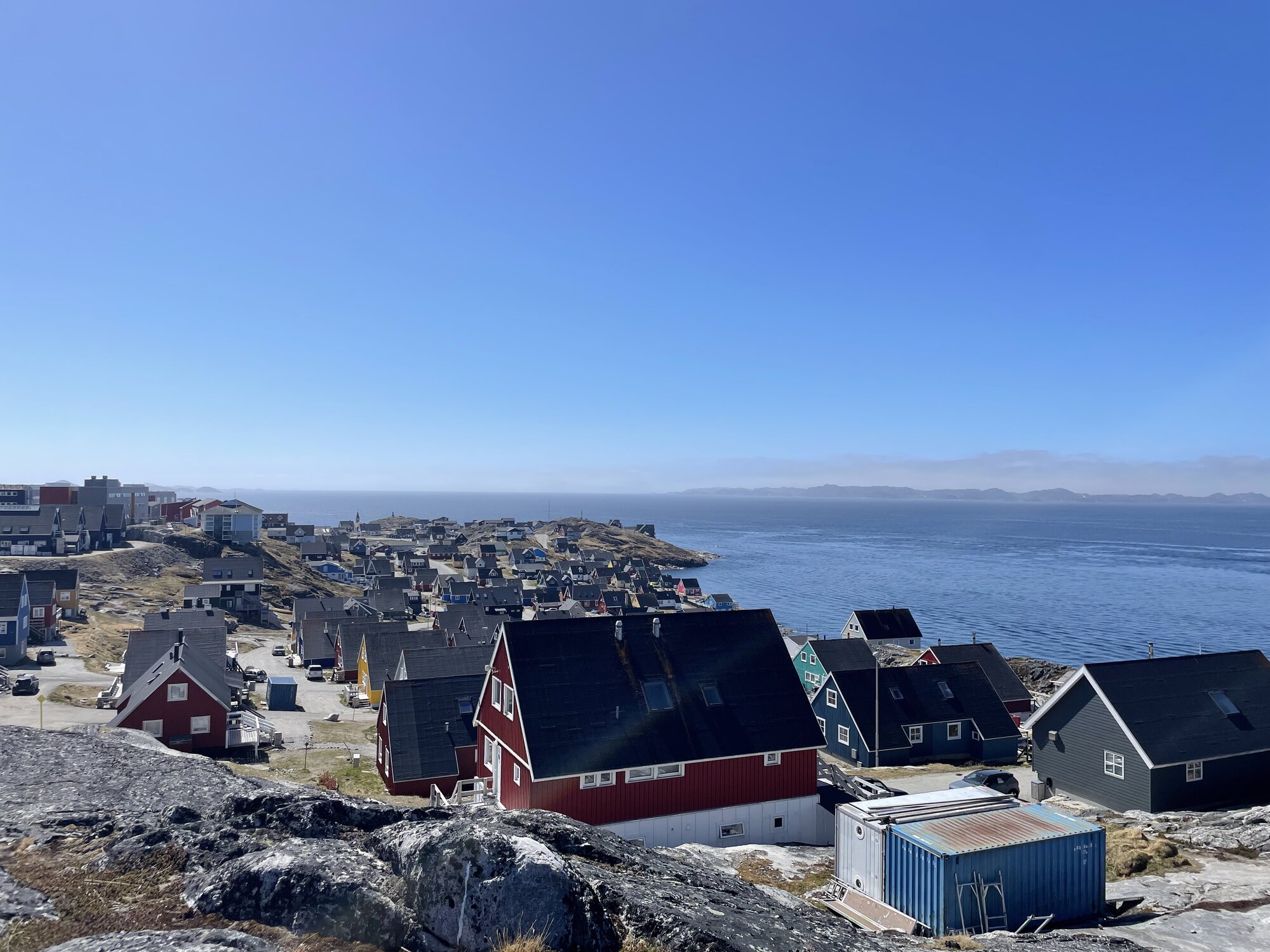 Farverige huse i Qernertunnguit set fra fjeldet med fjorden bag ved.